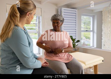 Fisioterapista femminile caucasica che tratta una paziente femminile americana afrcia anziana, copia spazio Foto Stock