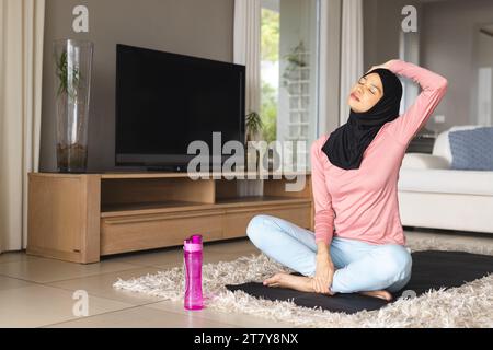 Donna birazziale in hijab che pratica yoga su materassino a casa Foto Stock