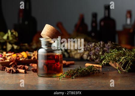 Tintura essenziale di erbe in una piccola bottiglia di vetro. Su un tavolo essiccavano erbe, fiori, spezie e vecchi utensili da cucina. Farmaco alternativo o complementare Foto Stock