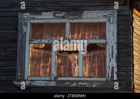 Una finestra nella casa di legno retroilluminata dal sole attraverso la finestra sull'altro lato della casa, regione di Arcangelo, Russia Foto Stock