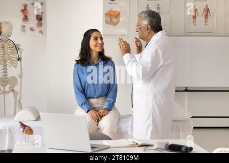 Uomo medico indiano anziano che esamina una giovane paziente positiva Foto Stock