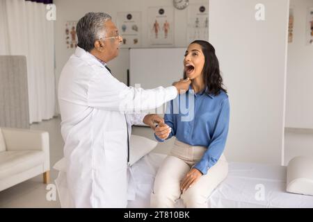 Grave medico indiano uomo che controlla i pazienti gola per influenza Foto Stock