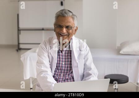 Allegro anziano medico indiano che indossa un cappotto bianco e occhiali Foto Stock