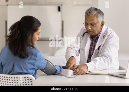 Uomo medico indiano anziano che controlla la pressione sanguigna di una giovane donna Foto Stock