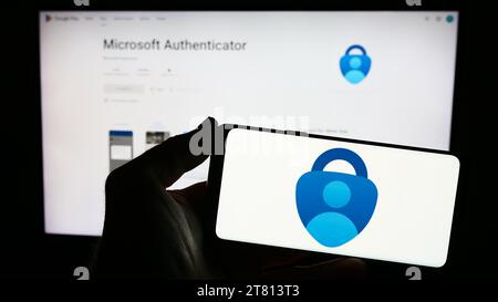 Persona che possiede uno smartphone con il logo dell'app di autenticazione Microsoft Authenticator davanti al sito Web. Concentrarsi sul display del telefono. Foto Stock