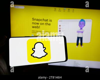 Persona che possiede il cellulare con il logo dell'app di messaggistica istantanea multimediale statunitense Snapchat davanti alla pagina Web dell'azienda. Concentrarsi sul display del telefono. Foto Stock