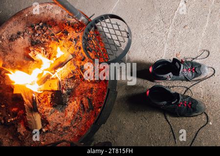 Un paio di scarponi da trekking si asciugano davanti a un fuoco con alcuni tronchi che bruciano all'interno di una capanna nel nord della Finlandia Foto Stock