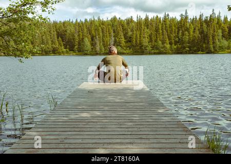 Un uomo si riposa alla fine di un molo privato durante una lunga escursione nella foresta in Finlandia Foto Stock