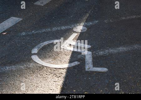 Cartello bianco per sedie a rotelle su un parcheggio asfaltato, indicante il posto riservato alle persone disabili Foto Stock