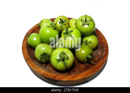 pomodori verdi in un piatto di legno, isolati su uno sfondo bianco Foto Stock