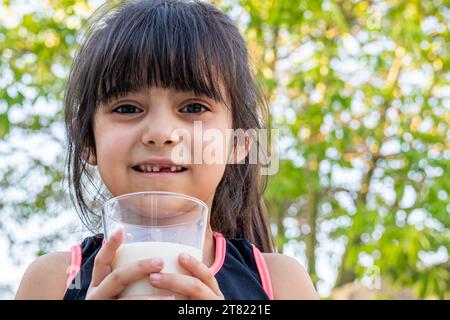 Ritratto ravvicinato di lei. Beve un bicchiere di latte freddo dopo aver giocato fuori casa sua. Foto Stock