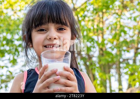 Ritratto ravvicinato di lei. Beve un bicchiere di latte freddo dopo aver giocato fuori casa sua. Foto Stock