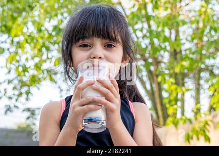 Ritratto ravvicinato di lei. Beve un bicchiere di latte freddo dopo aver giocato fuori casa sua. Foto Stock