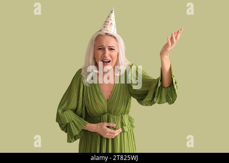 Sconvolta una donna matura con un cappello da festa su sfondo verde Foto Stock