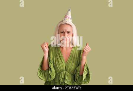 Donna matura scontenta in cappello da festa su sfondo verde Foto Stock