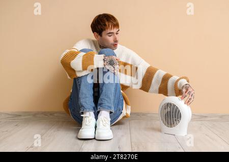 Giovane con riscaldamento elettrico seduto vicino al muro beige Foto Stock