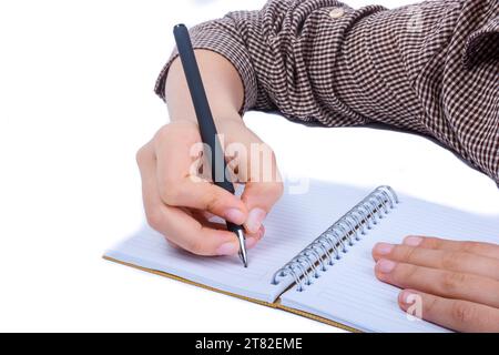 Un bambino è la mano scrivere con la penna su un notebook a spirale su sfondo bianco Foto Stock