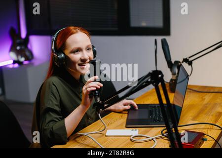 La presentatrice radiofonica parla nel microfono durante la trasmissione alla stazione radio. Blogger online durante lo streaming. Foto Stock