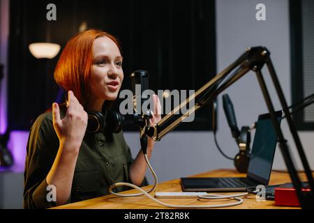 La presentatrice radiofonica parla nel microfono durante la trasmissione alla stazione radio. Blogger online durante lo streaming. Foto Stock