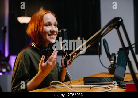 La presentatrice radiofonica parla nel microfono durante la trasmissione alla stazione radio. Blogger online durante lo streaming. Foto Stock