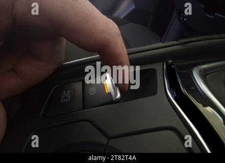 Il conducente tira il freno di stazionamento elettrico della sua auto. Spia di colore giallo che indica l'attivazione del freno in corso Foto Stock