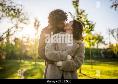 Felice coppia amorevole che si abbraccia e si bacia nel parco al tramonto. Foto Stock