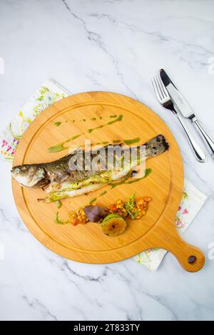 pesce al forno con lime e spezie su un vassoio di legno su uno sfondo di marmo, vista dall'alto Foto Stock