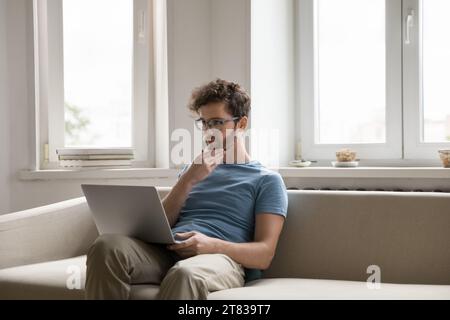 Un giovane concentrato lavora su un notebook a casa Foto Stock