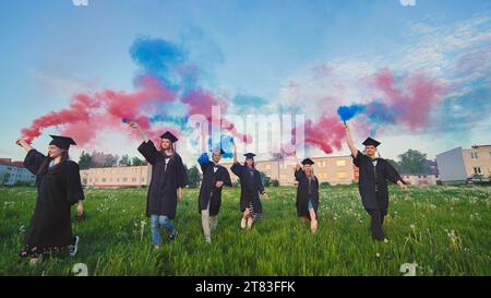 Gli studenti si laureano con fumo colorato che cammina attraverso il prato la sera. Foto Stock