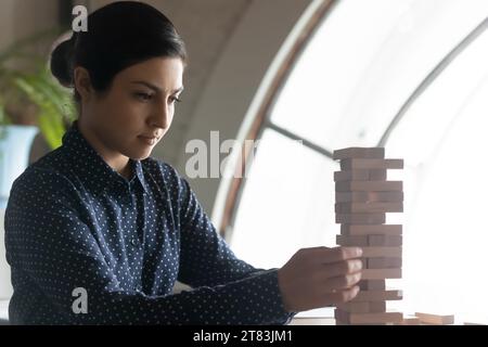 Donna d'affari indiana focalizzata, leader, project manager startup che gioca a jenga Foto Stock