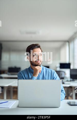 Uomo d'affari premuroso che pensa di lavorare su un notebook in ufficio. Shot verticale. Foto Stock
