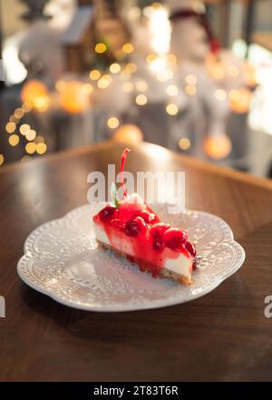 Fettine di cheesecake di fragole con strato di biscotti, ciliegia e marmellata in piatto bianco su un tavolo di legno Foto Stock