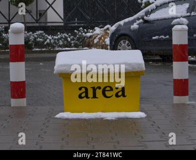 Una scatola gialla di sabbia ricoperta di neve tra le aste di parcheggio Foto Stock