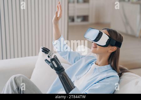 La donna sorridente con braccio bionico esplora la realtà virtuale, unendo tecnologia all'avanguardia e adattabilità umana Foto Stock