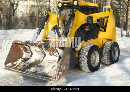 Attrezzatura per la raccolta della neve. Un trattore con benna. Rimozione della neve in città. Macchina per impieghi gravosi su cui lavorare. Foto Stock