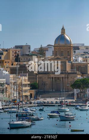 Le acque calme e le barche che circondano le tre città di fronte a la Valletta a Malta - Kalkara Village Parish Church Silver Dome Buildings Foto Stock