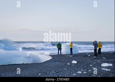 I turisti che camminano lungo la riva di Breiðamerkursandur, o Diamond Beach, vicino alla laguna di Jokulsarlon, con iceberg lavati sulla costa, l'Islanda Foto Stock