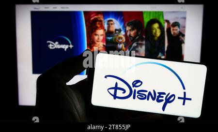 Persona che possiede uno smartphone con il logo del servizio di streaming video on demand degli Stati Uniti Disney Plus davanti al sito Web. Concentrarsi sul display del telefono. Foto Stock
