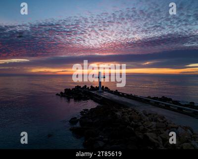 Un volo intorno a una croce cristiana la mattina presto all'alba. La grande croce sorge sul bordo di un frangiflutti sulla costa del mare. Foto Stock