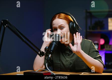 Giovane donna adulta moderna che indossa cuffie per registrare podcast o trasmettere in studio domestico. Foto Stock