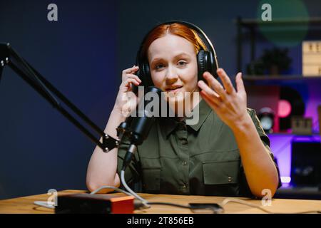 Giovane donna adulta moderna che indossa cuffie per registrare podcast o trasmettere in studio domestico. Foto Stock