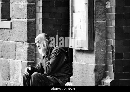 Brecon, Powys, Galles 22 ottobre 2023: Vecchio senzatetto dai capelli grigi con barba piena seduto all'ingresso degli uffici del Consiglio della Guild Hall. Foto Stock