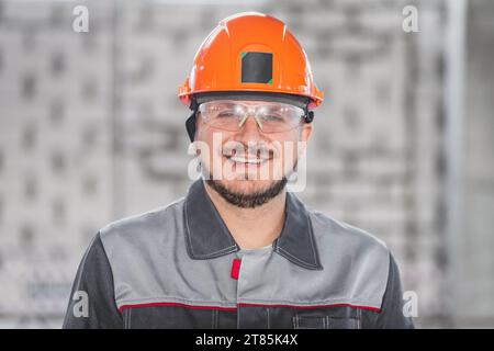 Ritratto di operaio edile, uomo caucasico in elmetto, occhiali protettivi e uniforme, costruzione e ispezione Foto Stock