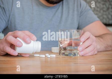 Uomo seduto in cucina con un bicchiere d'acqua per prendere le sue pillole. Foto Stock