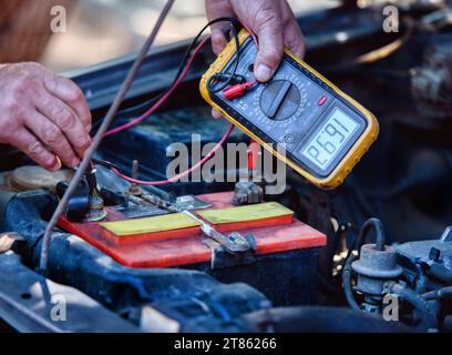 manutenzione elettrica dell'auto, elettricista con un misuratore che misura la tensione su una batteria dell'auto vecchia Foto Stock
