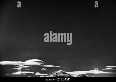 Una fotografia di paesaggio in bianco e nero cattura un cielo spettacolare sopra una catena montuosa, con nuvole lenticolari che sorvolano le vette. Foto Stock