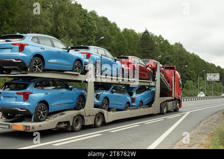 Trasporto di autoveicoli. Il veicolo trasporta le auto su un rimorchio. Autostrada fuori città. Molte auto sulla piattaforma. Foto Stock