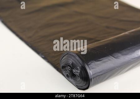 Una foto di una fodera di un contenitore nero rotolata su una superficie bianca. Foto Stock
