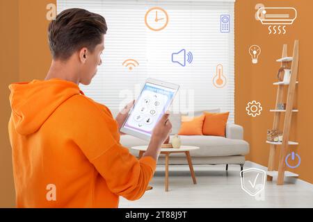 Uomo che utilizza un sistema di controllo intelligente della casa tramite applicazione su tablet in interni. Diverse icone vicino a lui Foto Stock