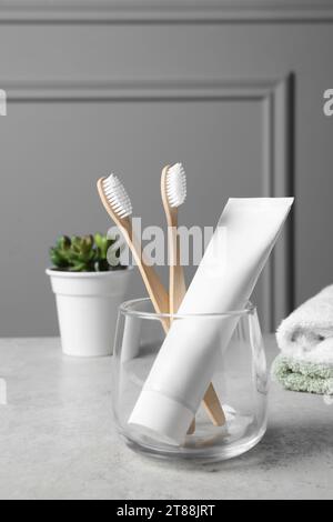 Spazzolini da denti di bambù nel supporto, dentifricio, piante domestiche e asciugamani su tavolo grigio chiaro Foto Stock